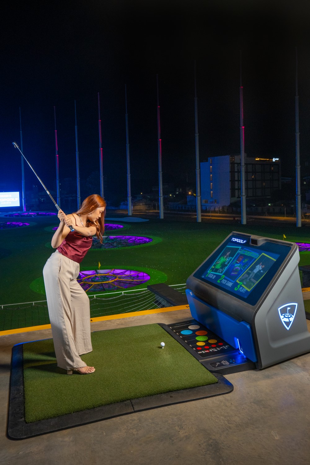 Seorang wanita mengayunkan tongkat golf di bay Topgolf.